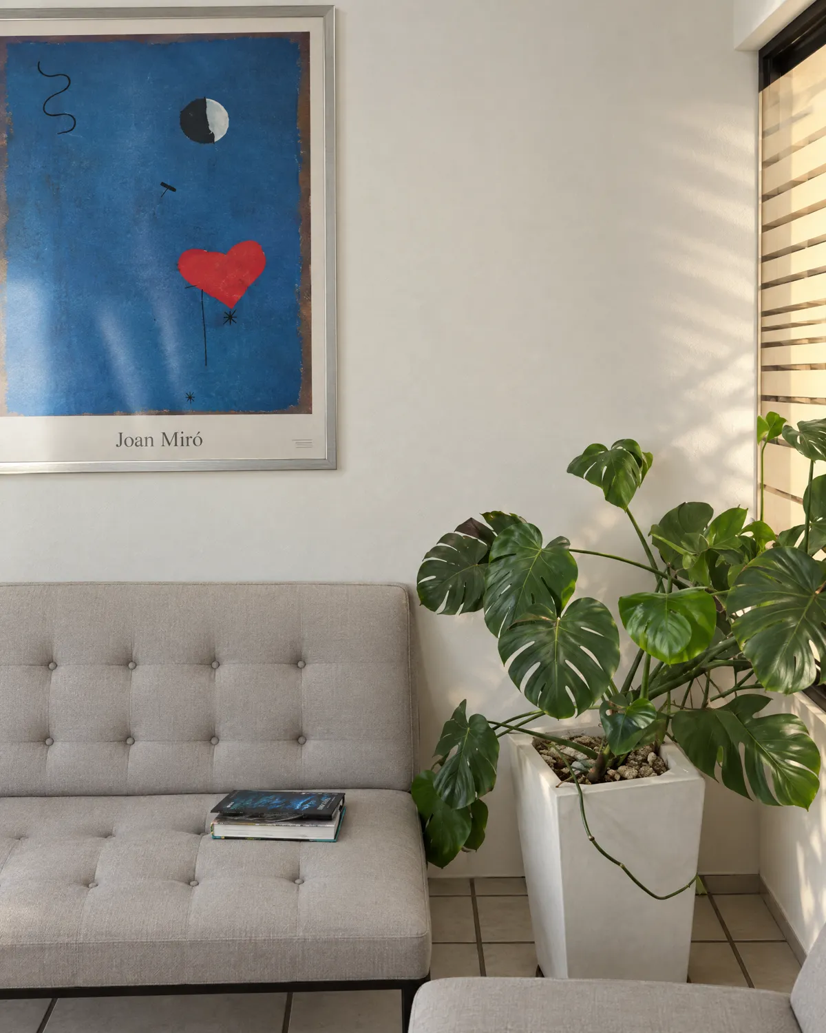 Waiting room: tufted loveseat, a monstera and a Joan Miró poster